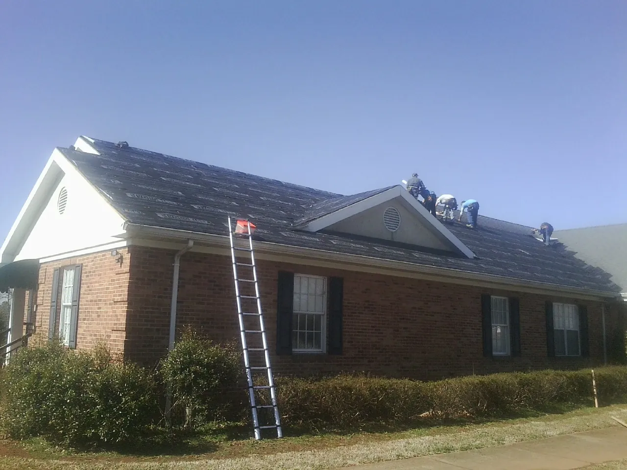 Crew tearing shingles off a brick ranch roof with a ladder set — Metal Roof Repair work by our crew in Saint Helens