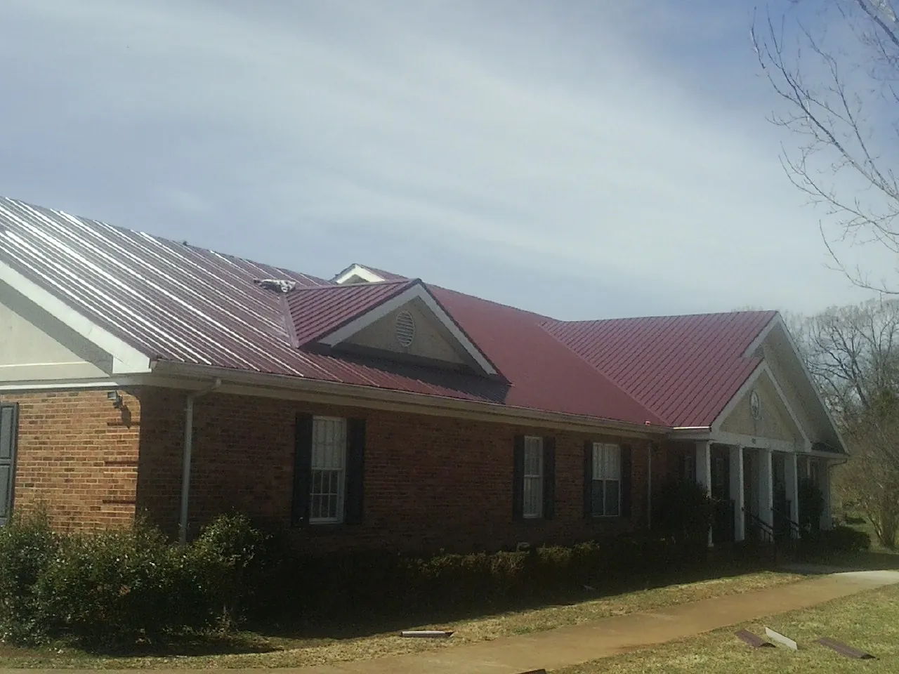 Red metal roof with gabled entries on a long brick building, from a Hail Damage Roof Repair job in Saint Helens