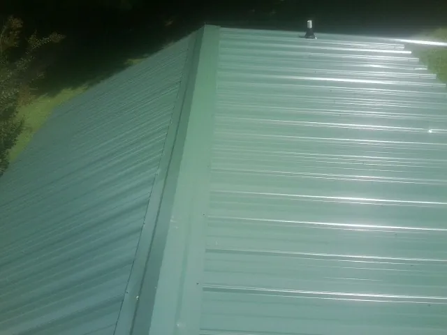 New green metal panels meeting at the ridge of a roof — Flat Roof Repair work by our crew in Saint Helens
