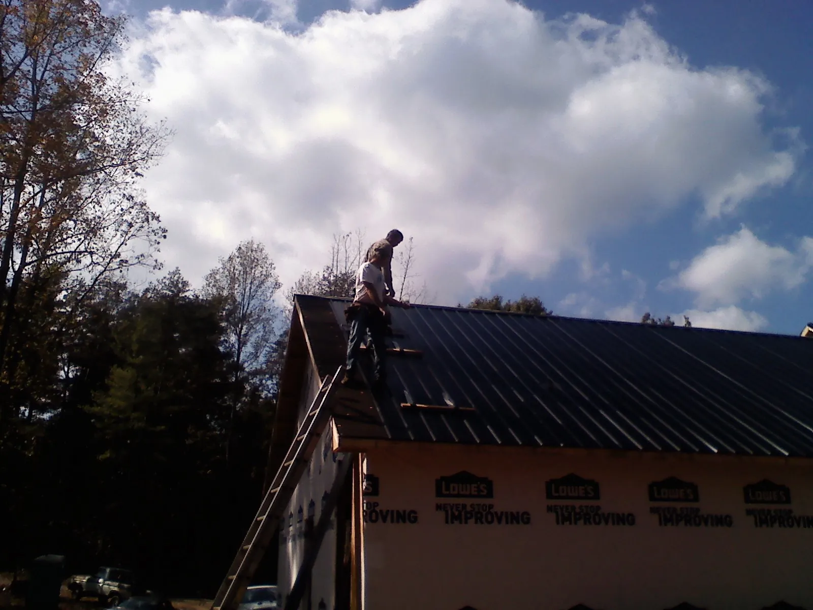 Roofer fastening dark metal panels high against a cloudy sky, from a Roof Inspection job in Saint Helens