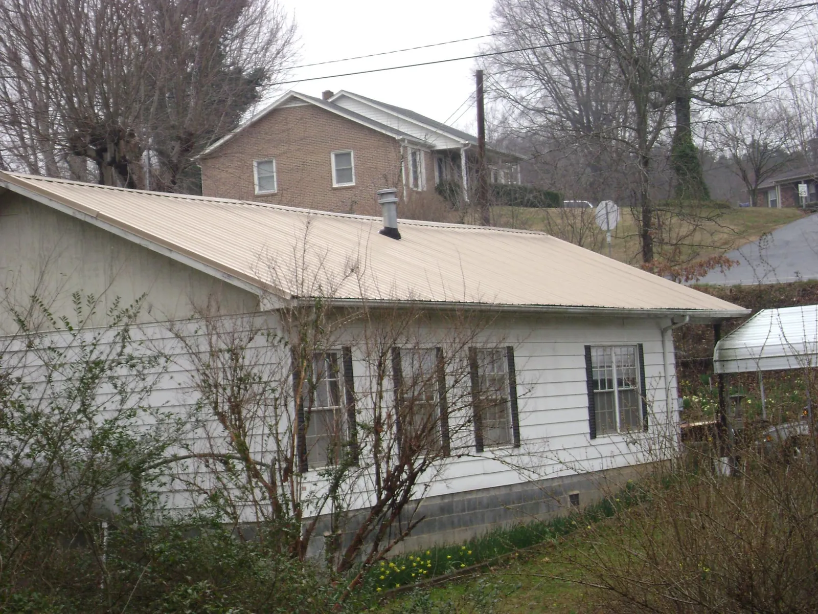 Tan metal roof on a white sided house set into a hillside — Commercial Roofing by Roofing Brothers in Saint Helens